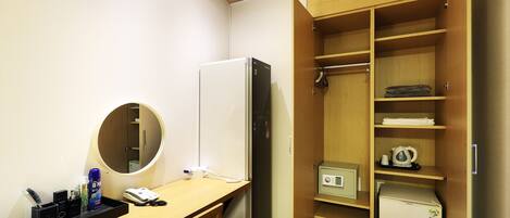 A hotel room with a wooden desk, a refrigerator, a microwave, a safe, and a wardrobe with shelves.