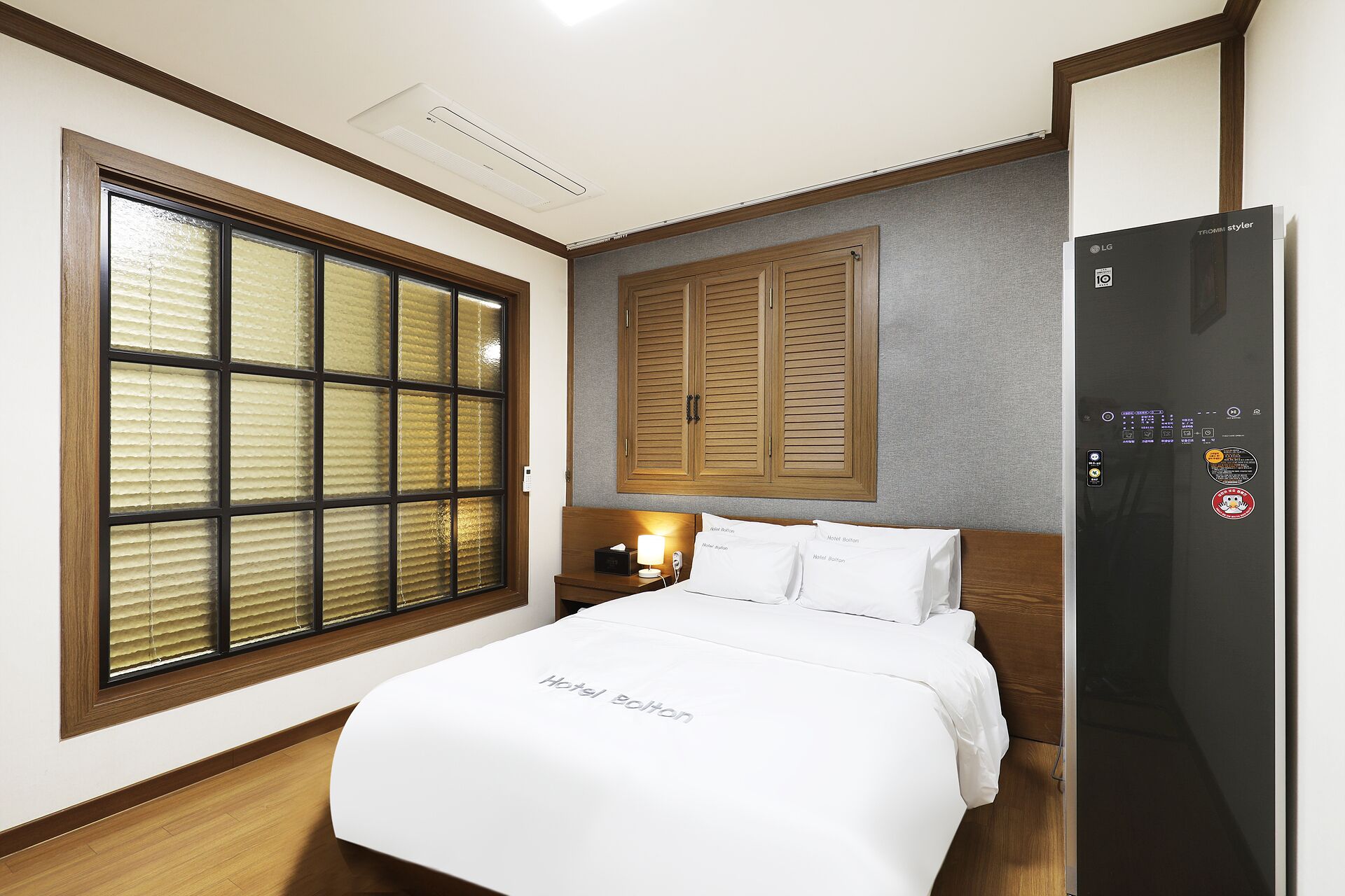 A hotel room with a bed, a nightstand, a lamp, a wardrobe, and a built-in refrigerator.