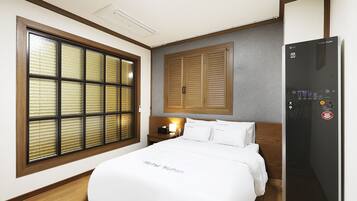 Habitación de hotel con cama, mesita de noche, lámpara, armario y refrigerador incorporado.