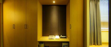 A hotel room with a wooden wardrobe, a bench with a small table, and a window with curtains.
