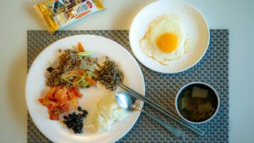 A meal with rice, kimchi, and a fried egg on a plate, accompanied by a packet of snacks and a bowl of soup.