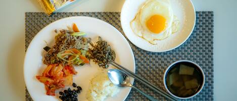 A meal with rice, kimchi, and a fried egg on a plate, accompanied by a packet of snacks and a bowl of soup.