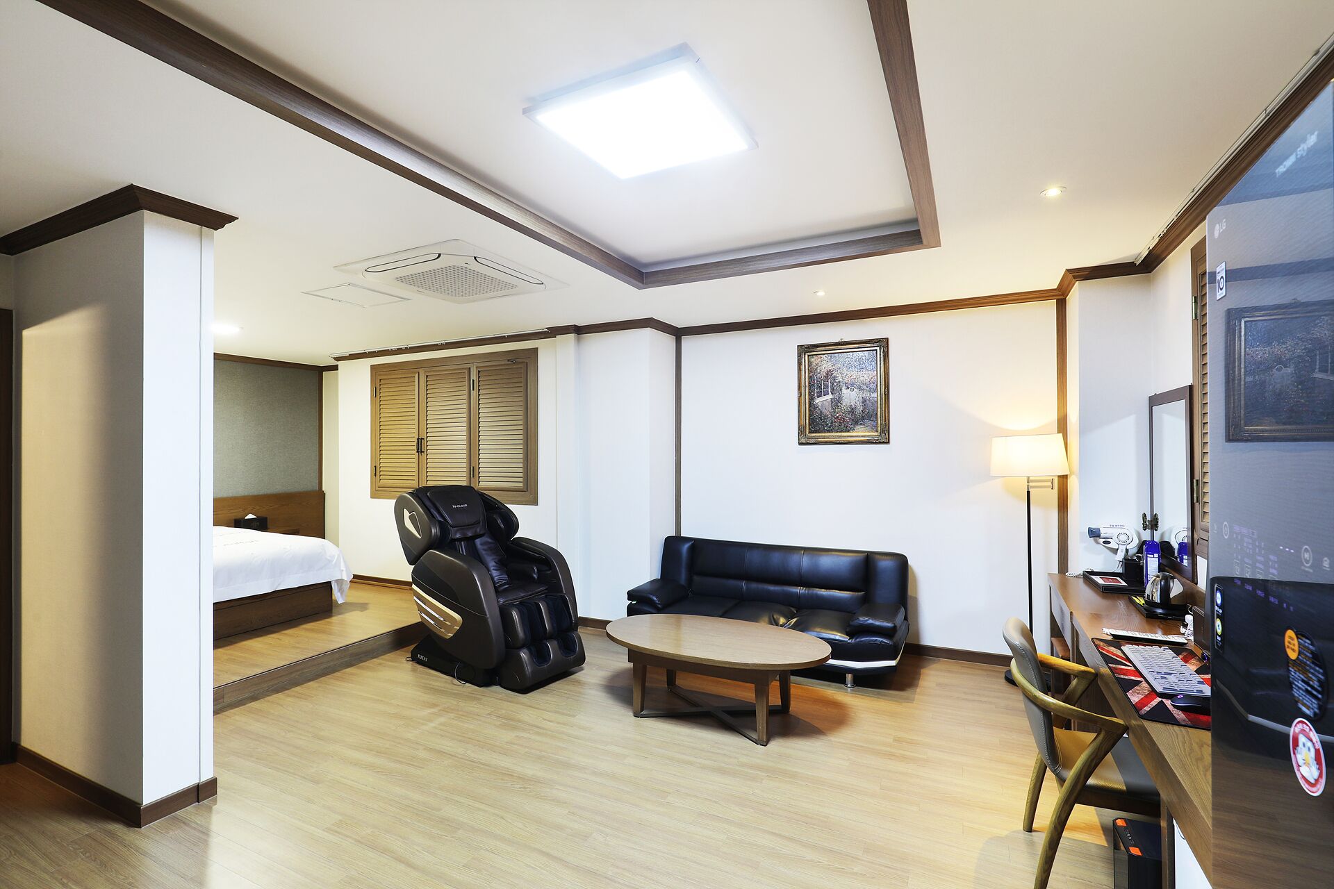 A hotel room with a bed, massage chair, sofa, and a desk with a computer.
