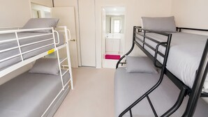 A room with bunk beds, a bathroom with a mirror, and a door leading to another room.