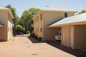 A residential area with brick buildings, a paved walkway, and a parked white van. - Midland Haven - Midland WA (Midland)