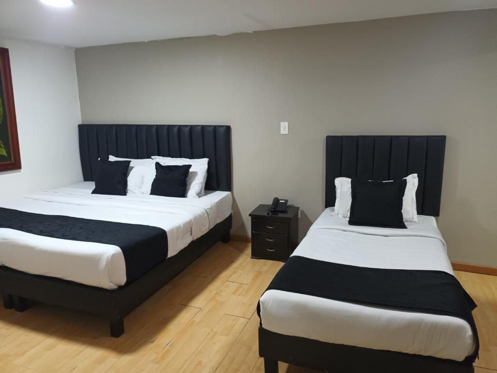 Dos camas con cabeceros negros, ropa de cama blanca y una mesita de noche con un teléfono.