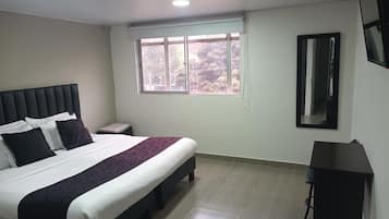 Un dormitorio con cama, mesita de noche, ventana y escritorio.