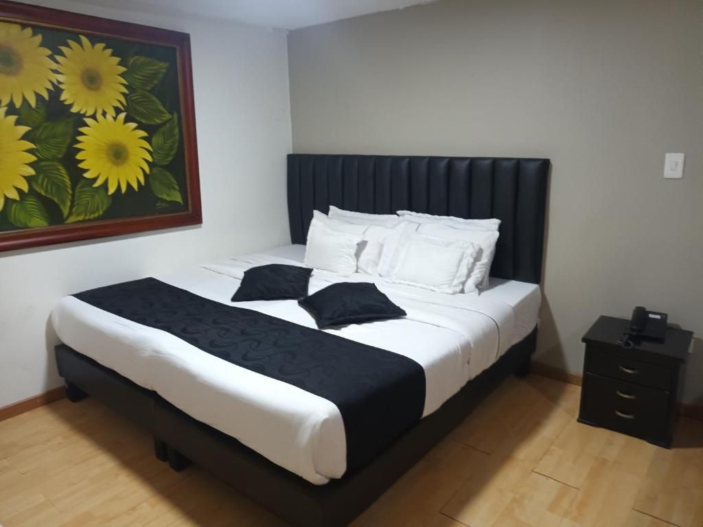 A neatly made bed with white and black bedding, a dark headboard, and a painting of sunflowers on the wall.
