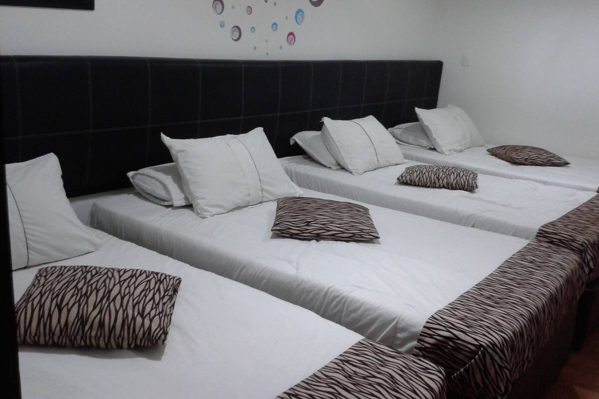 Habitación de hotel con cuatro camas individuales, cada una con ropa de cama blanca y almohadas estampadas.
