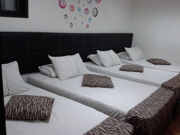 Habitación de hotel con cuatro camas individuales, cada una con ropa de cama blanca y almohadas estampadas.