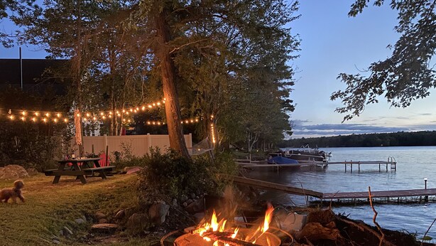 A fire pit with a metal grill, surrounded by rocks and a small bowl of wood. - Waterfront Lakefront Cottage, Sleeps 6. Parking.  (Old Town)