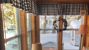 A cozy room with a checkered ceiling, a wooden table with a globe and books, a patterned sofa, and a window with a view of a snowy landscape. - Waterfront Lakefront Cottage, Sleeps 6. Parking.  (Old Town)