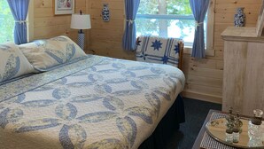 A wooden cabin room with a bed, a desk, a lamp, and a window with curtains. - Waterfront Lakefront Cottage, Sleeps 6. Parking.  (Old Town)