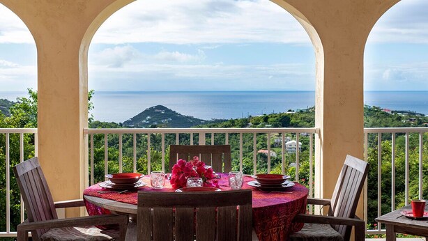 A dining area with a table set for two, overlooking a scenic view of the sea and greenery.