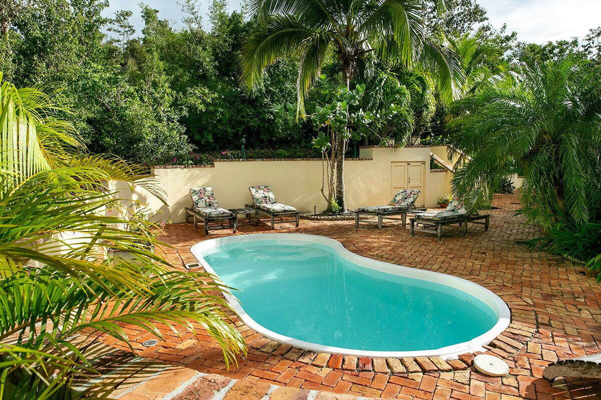 A swimming pool with lounge chairs, surrounded by lush greenery and a brick patio.