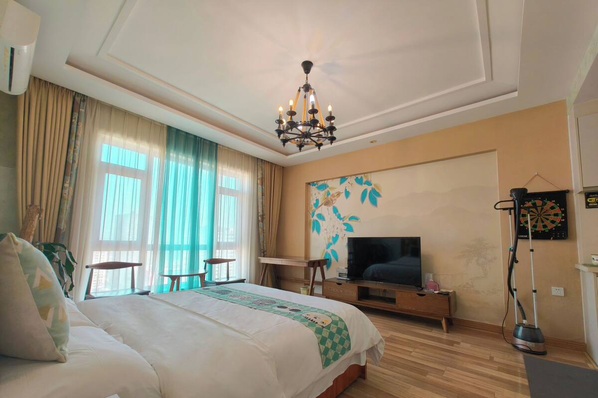 Ein Hotelzimmer mit einem großen Bett, einem Fernseher, einem Schreibtisch und einer an der Wand befestigten Dartscheibe.
