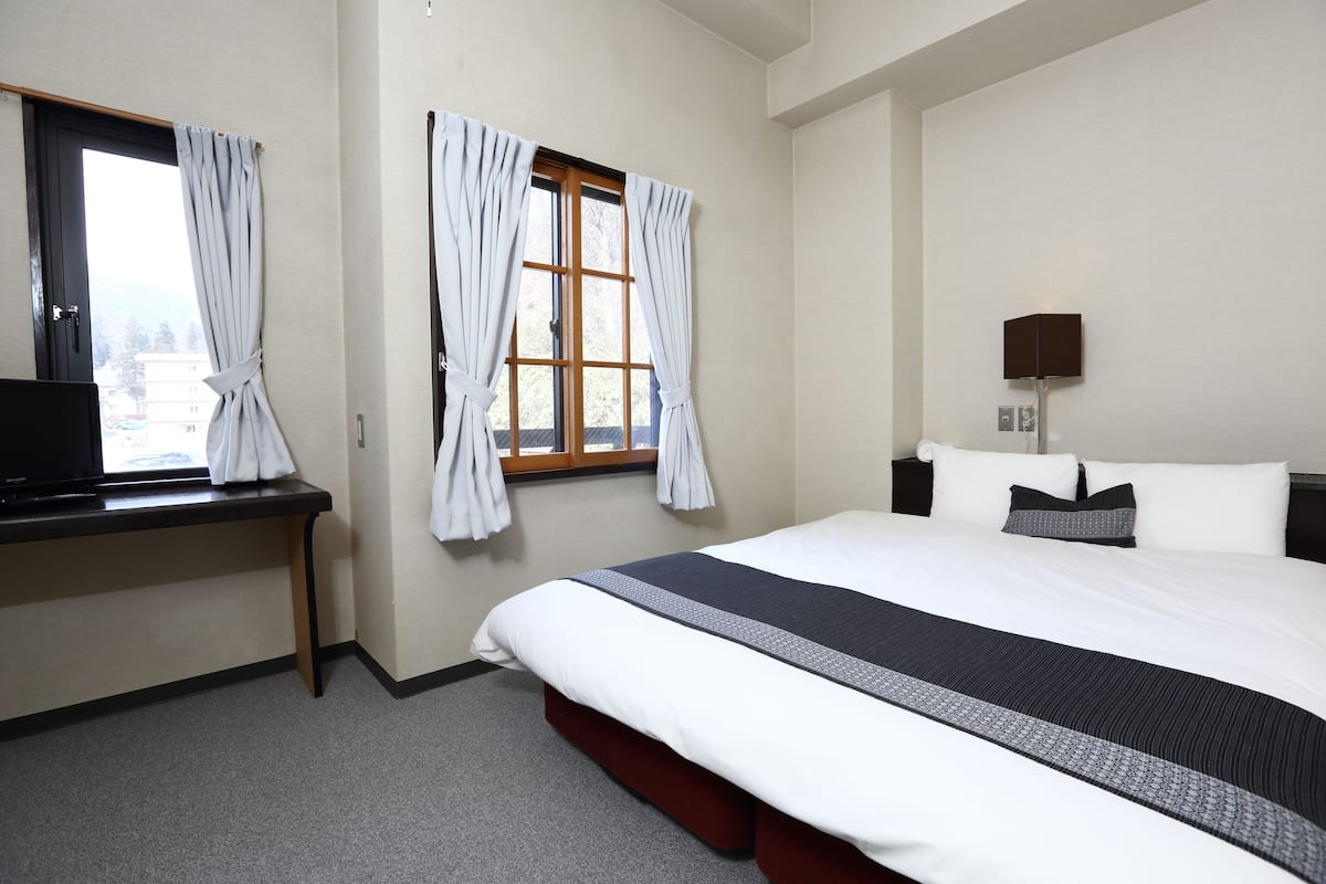 A hotel room with a bed, a desk, a lamp, and curtains on the windows.