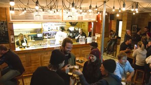 Un bar con mostrador, taburetes y clientes.