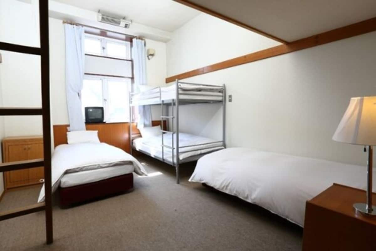 A room with bunk beds, a wooden wardrobe, a bedside table with a lamp, and a window with curtains.