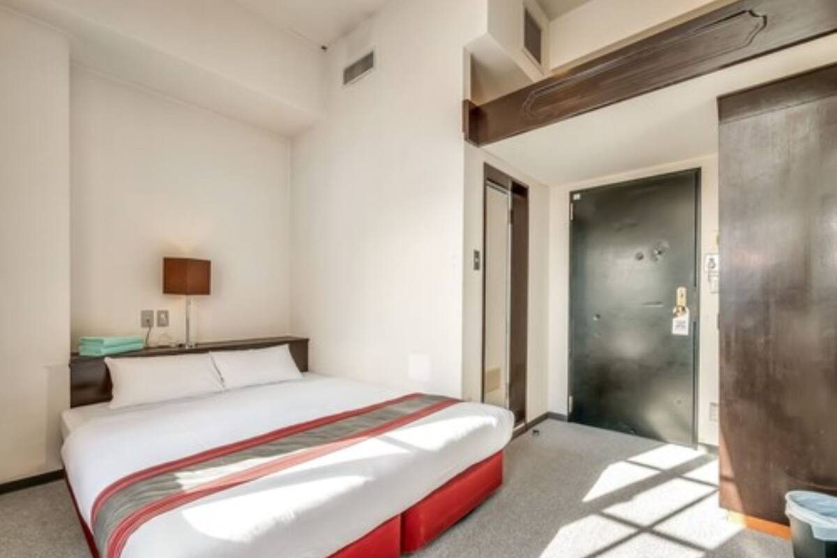 A hotel room with a bed, a nightstand, a lamp, and a door.