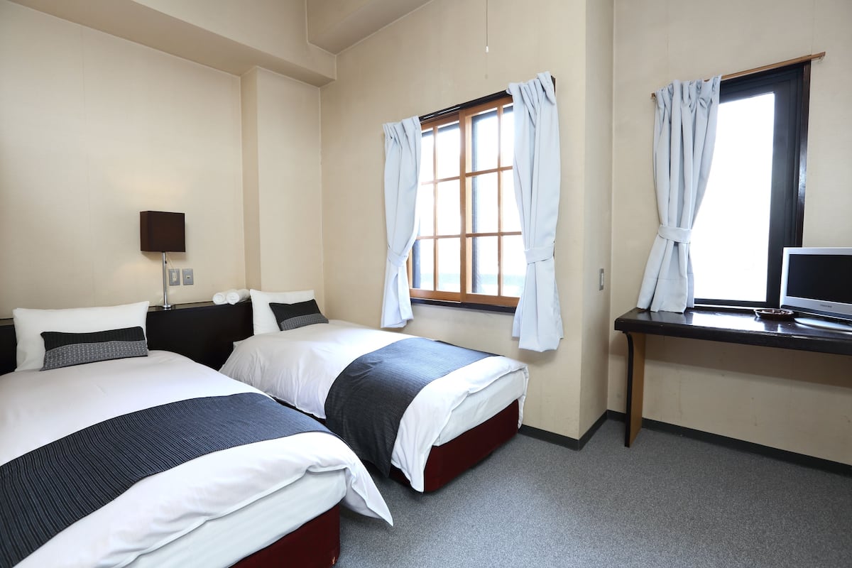A hotel room with two beds, a desk with a computer, and a window with curtains.