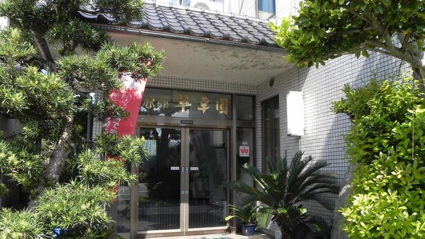 Ein traditionelles japanisches Gebäude mit einem Ziegeldach, einem Glastürbereich und einem kleinen Garten mit Topfpflanzen und einem Kiesweg.