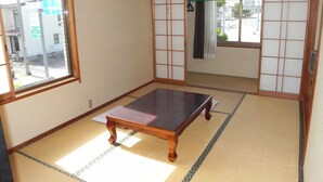 Ein traditioneller japanischer Raum mit Tatami-Böden, einem niedrigen Holztisch, gleitenden Shoji-Schiebetüren und Blick auf die Straße.