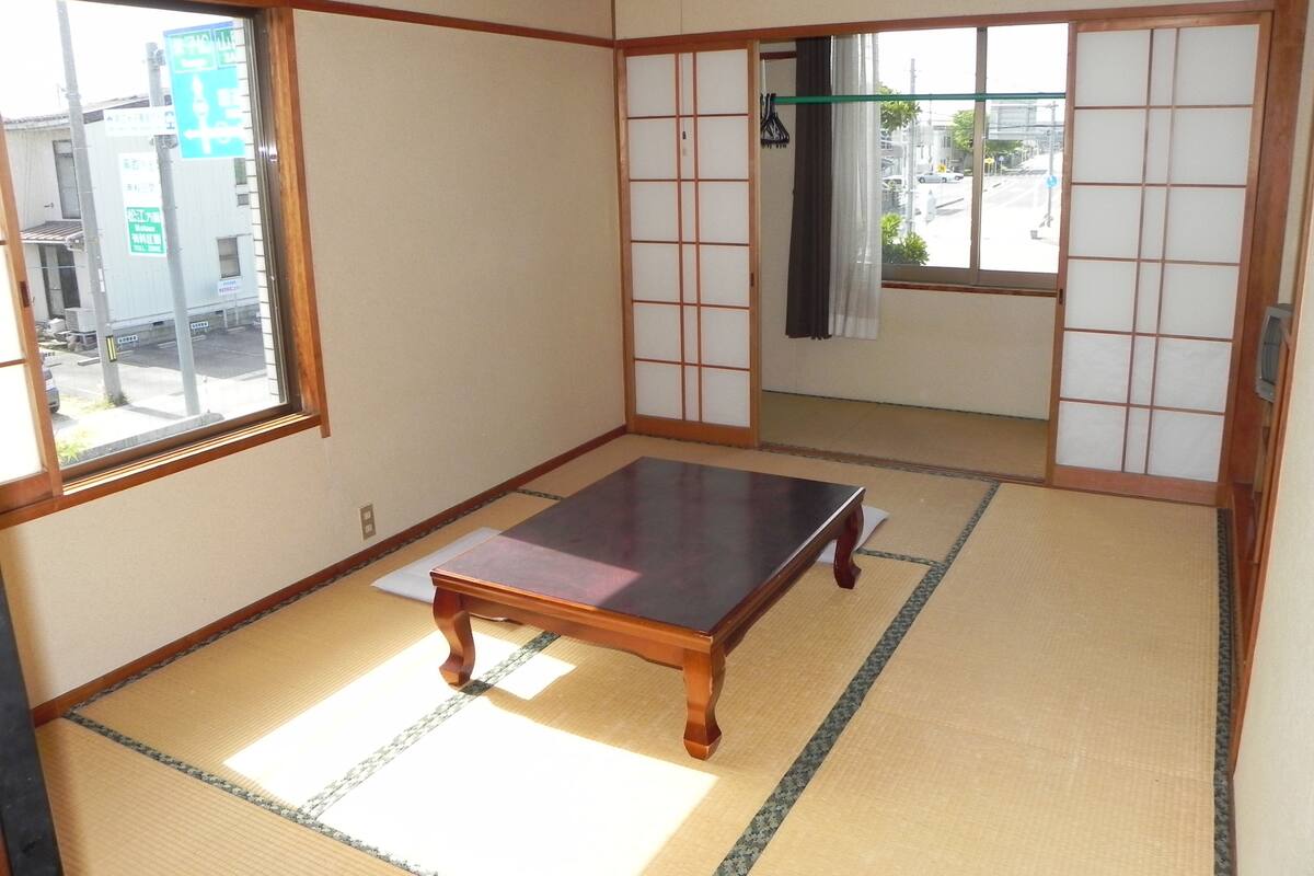 Une pièce de style japonais traditionnel, avec un sol recouvert de tatamis, une petite table en bois, des portes coulissantes en papier de riz (shoji) et une vue sur la rue.