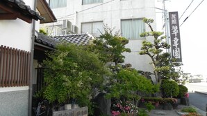 Ein traditionelles japanisches Gebäude mit einem Ziegeldach, umgeben von üppigem Grün und einem Schild, das einen Parkplatz kennzeichnet.
