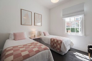 Een hotelkamer met twee bedden, een raam met uitzicht en twee ingelijste bladerkunstwerken aan de wand.