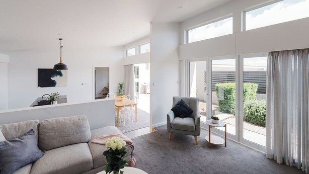 Amplia sala de estar con un sofá, sillón y una pequeña mesa.  Zona de comedor con mesa y sillas, y vistas al exterior a través de grandes ventanales.