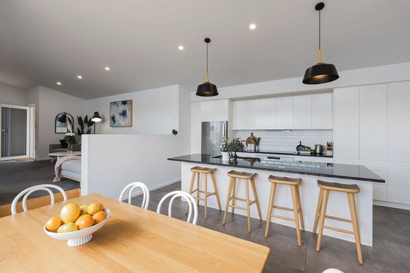 Een moderne keuken met witte kasten, een zwart aanrecht en houten krukken.