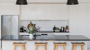Una cocina moderna con gabinetes blancos, un refrigerador de acero inoxidable, una encimera negra y taburetes de madera.