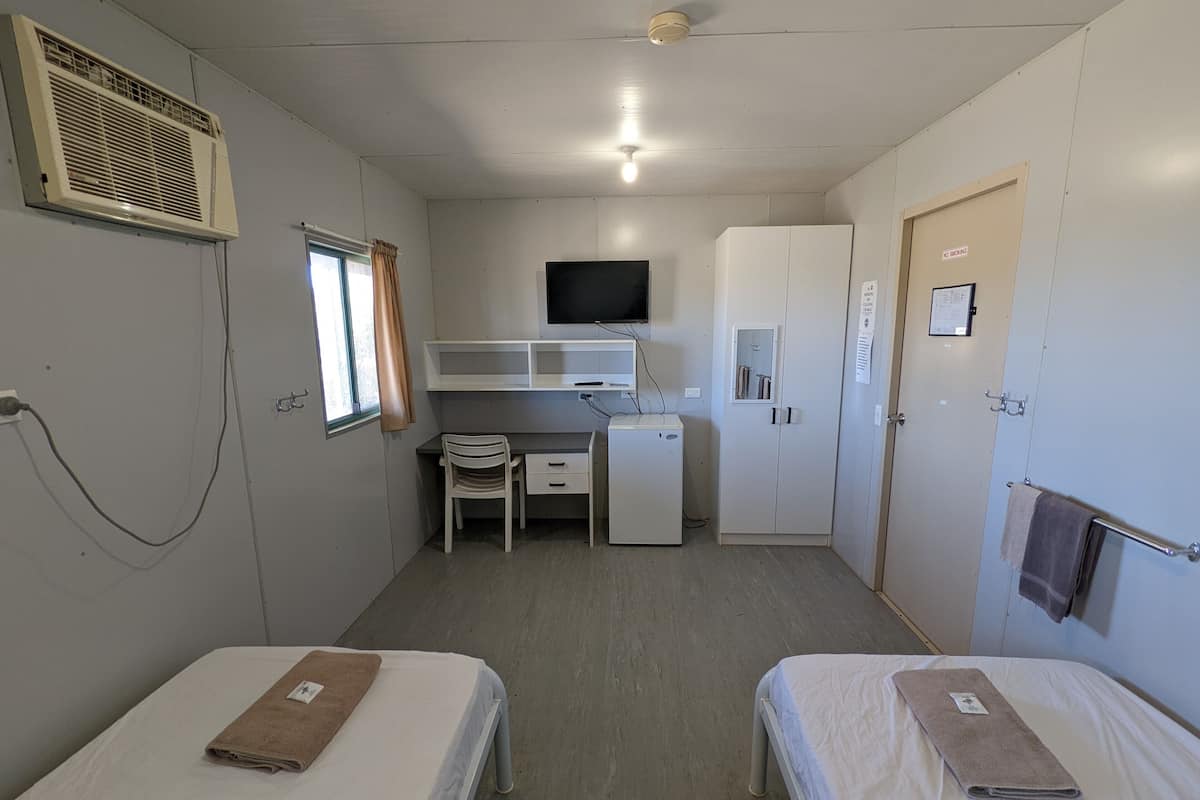 Habitación compacta con dos camas, un escritorio, un refrigerador pequeño, un televisor y un armario.