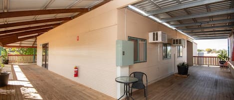 Un espacio al aire libre techado con una terraza de madera, una mesa con sillas y un extintor.