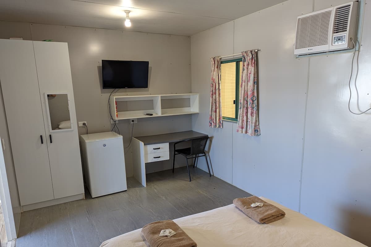 Una habitación pequeña con cama, escritorio, armario, televisor y aire acondicionado.