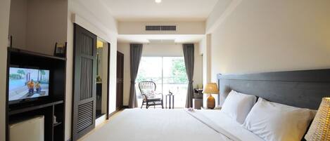 A hotel room with a large bed, a TV on a stand, a chair, a small table, and a lamp.