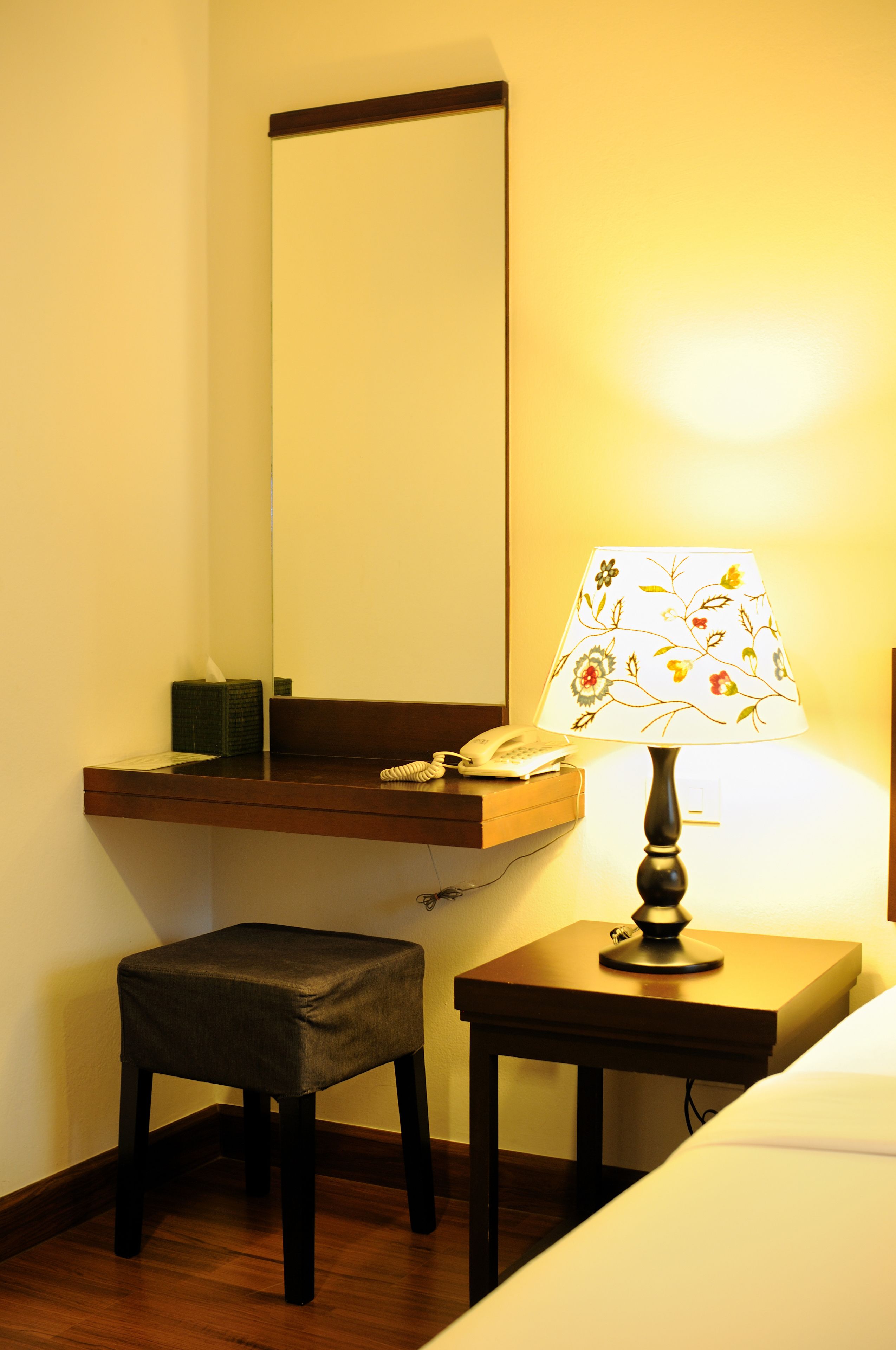 Ein kleiner Raum mit Schreibtisch aus Holz, Stuhl, Lampe, Telefon und Spiegel.