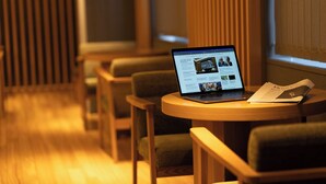 A laptop on a round table with a magazine, in a room with wooden flooring and green upholstered chairs.