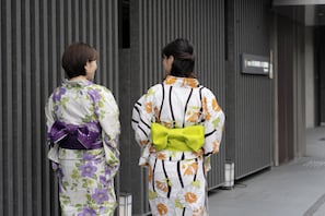 Two individuals in traditional attire walking past a building with vertical lines and a sign. - Hotel Vista Premio Kyoto Nagomitei (Kyoto)