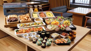 A buffet table with various food items and beverages, including a box of fresh hot pancakes, salads, and sushi.