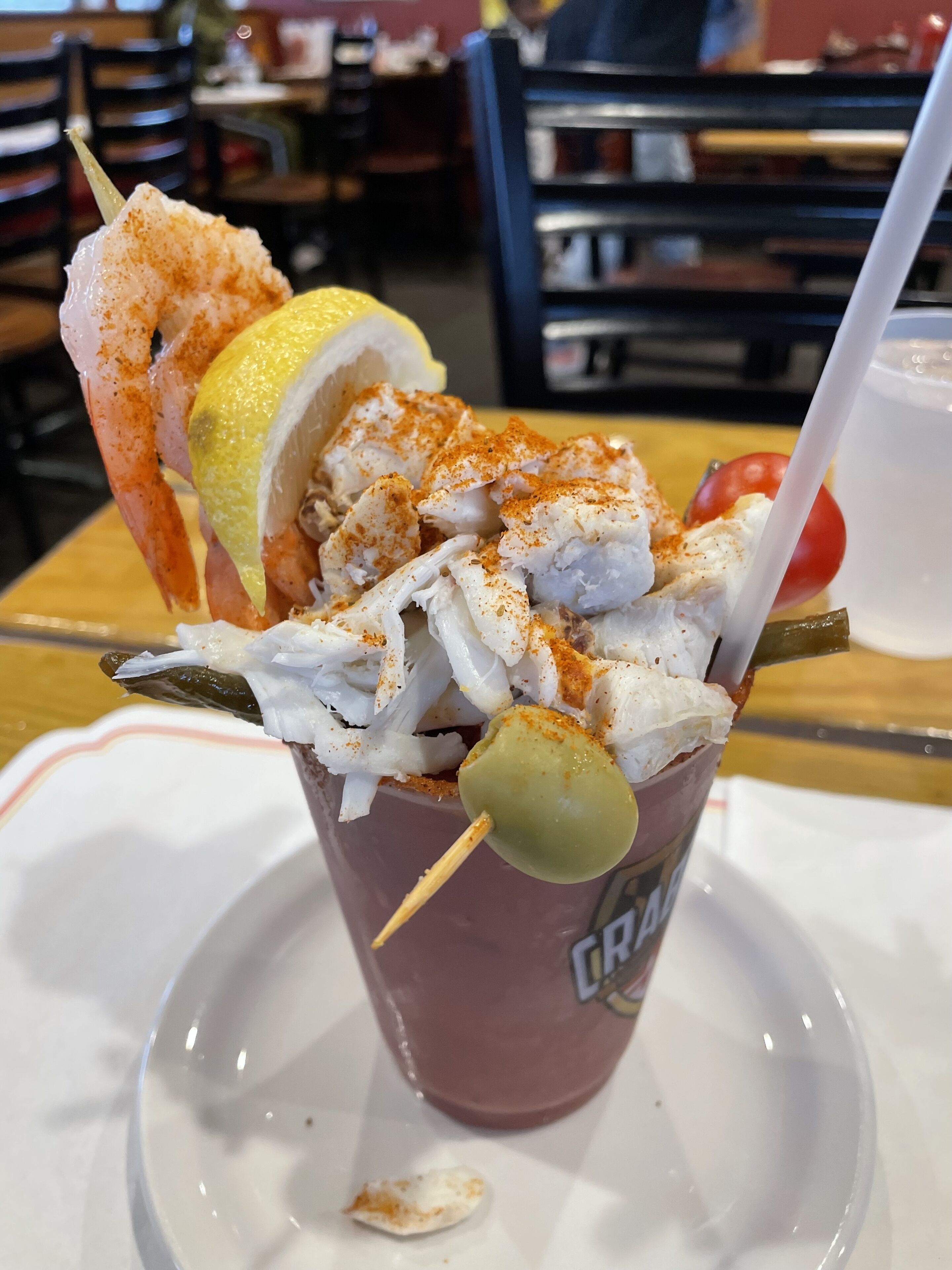 A beverage with a lemon wedge, a cherry, and a skewer with food items on a cup.