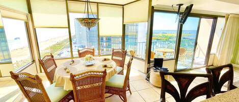 Un comedor con sillas de mimbre y una mesa dispuesta para cuatro, ventanas amplias con persianas y vistas a la ciudad.