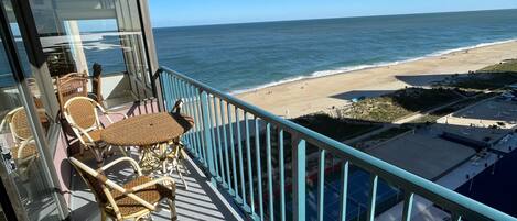 A balcony with wicker furniture overlooking a beach.