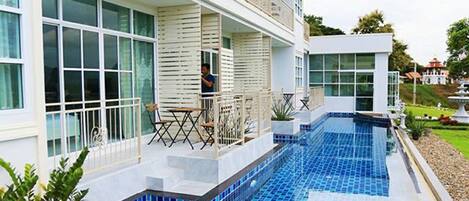A modern hotel with a large outdoor swimming pool, multiple balconies, and a well-maintained garden area.