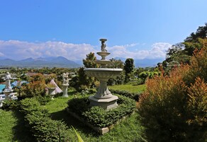 Un jardín con una fuente central, rodeado de estatuas y abundante vegetación.