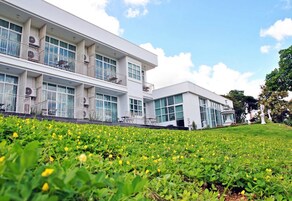 Un edificio moderno con varios balcones y ventanas amplias, rodeado de un césped bien cuidado con flores amarillas.