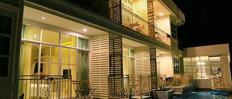 Un hotel moderno con piscina en la azotea, ventanas amplias y un balcón con mobiliario de exterior.