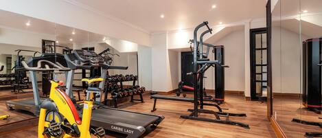 Un gimnasio amplio con máquinas de cardio, pesas libres y un espejo grande.