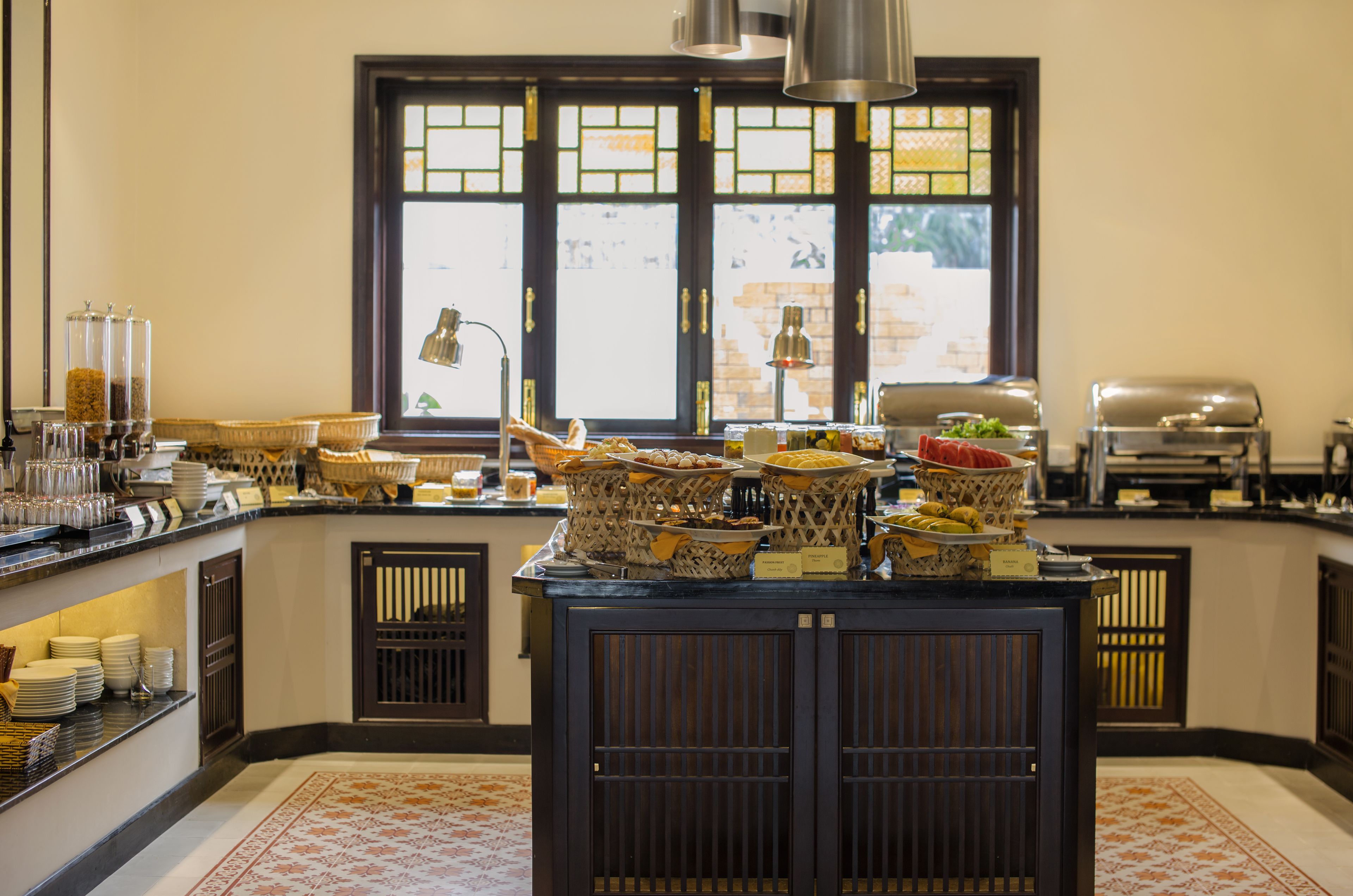 A buffet setup with various food items and utensils, a window with decorative panes, and a kitchen area with appliances.